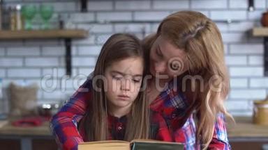 美丽的年轻妈妈在为坐在厨房桌子旁的一个可爱的小女儿读一本书。 孩子很<strong>难过</strong>